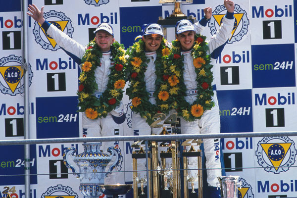 Allan McNish, Stéphane Ortelli, Laurent Aiello auf dem Podium vor einem Mobil 1-Logo in Le Mans 1998