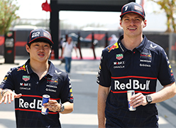 Max Verstappen und Yuki Tsunoda gehen mit Red-Bull-Dosen in der Hand spazieren und unterhalten sich.