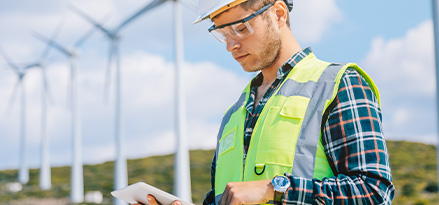 Ingenieur steht vor Windturbinen und arbeitet an seinem Tablet