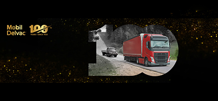 Altes Fahrzeug fährt hinter modernem, rotem LKW auf Autobahn mit goldenem Glanz