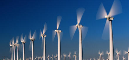 Reihe weißer Windturbinen, die über eine trockene, grasbewachsene Ebene vor klarem blauem Himmel rotieren