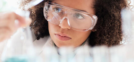Wissenschaftlerin mit Schutzbrille untersucht sorgfältig einen Kolben im Labor