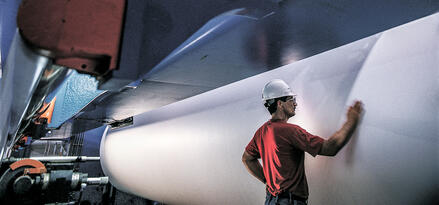 Fabrikarbeiter mit Schutzhelm inspiziert eine große Papierrolle in einer industriellen Druckmaschine